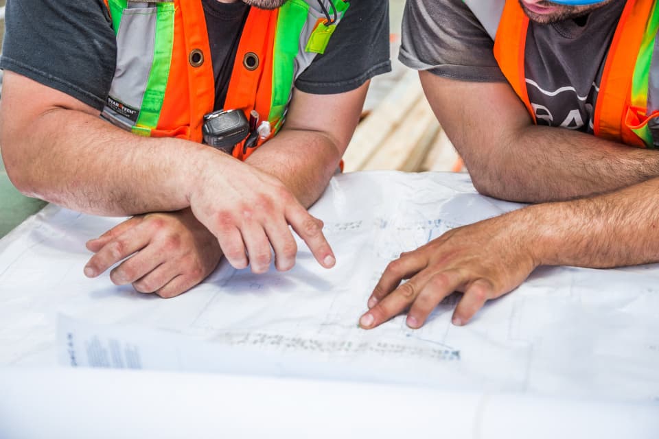 Construction crew in safety vests reviewing blueprints together